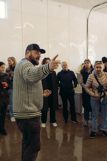 A person gesturing in a room with a group of people standing in the background. 4
