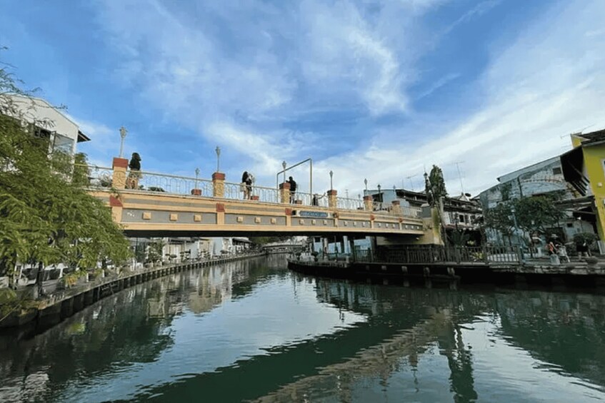 A bridge over a calm river with buildings on either side, a clear sky, and a reflection of the bridge in the water. 5