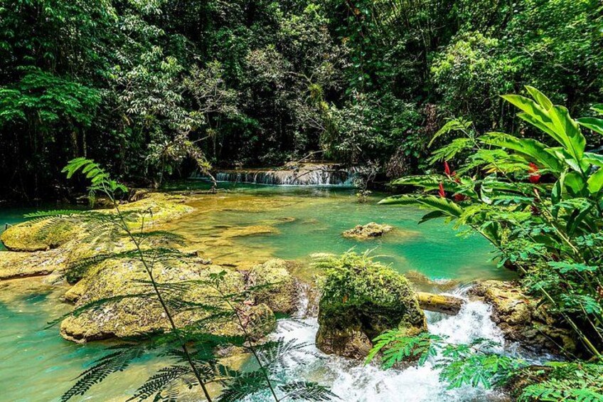 A clear turquoise river with rocks, lush greenery, and a waterfall. 2
