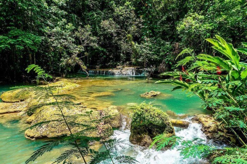 A clear turquoise river with rocks, lush greenery, and a waterfall. 5