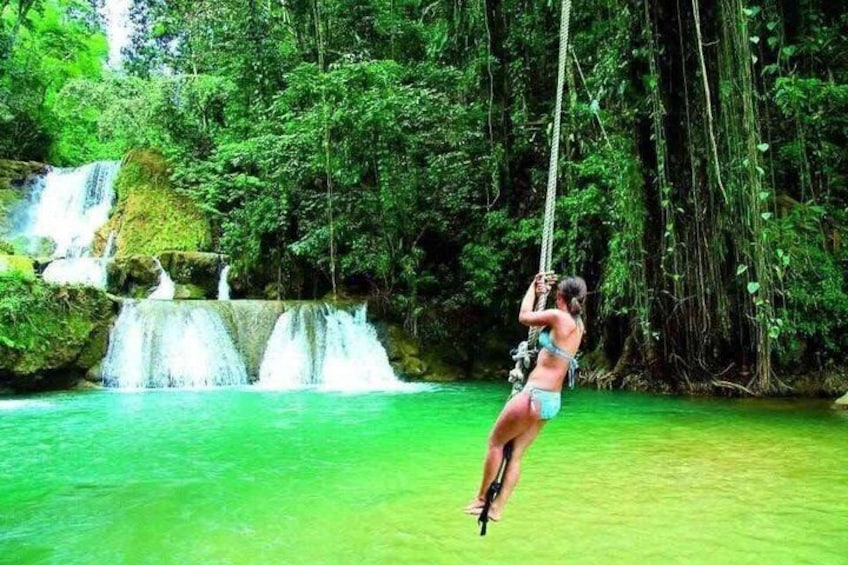 A person swinging on a rope in a forest with waterfalls and a green river. 1
