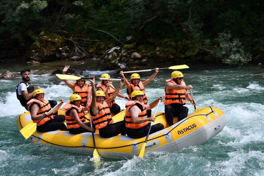 A group of people in a yellow inflatable raft on a river, wearing life jackets and helmets. 1