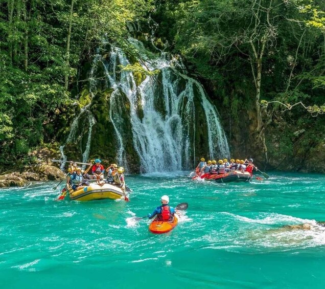 A group rafting on a turquoise river with a waterfall in the background. 4