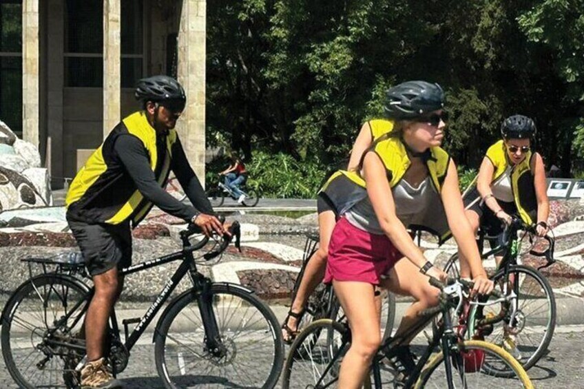 Three cyclists wearing reflective vests riding bicycles on a paved path. 5
