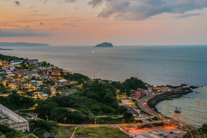 A coastal town at dusk with a winding road, buildings, and a distant island. 2