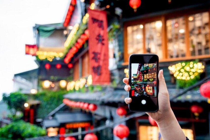 A hand holding a smartphone with a photo of a traditional building with red lanterns and a red banner. 5