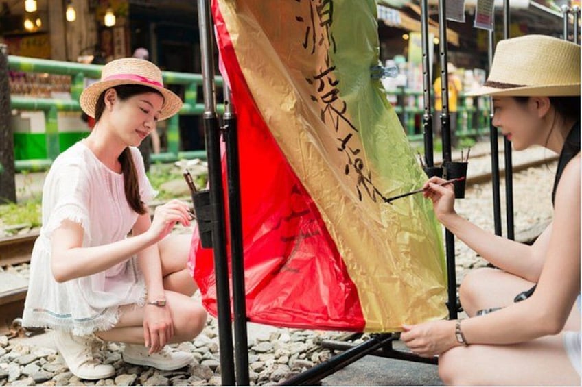 Two individuals painting a large, colorful flag on a metal frame. 4