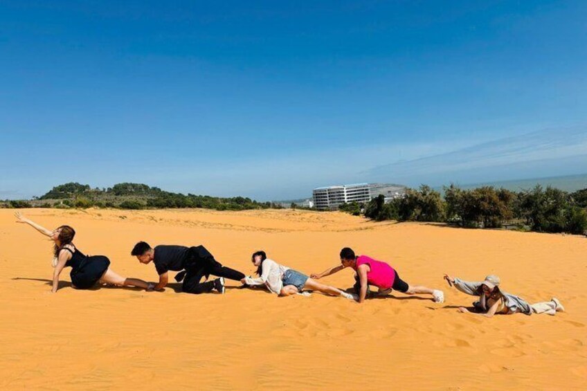 A group of people stretching on a sandy beach with a clear sky and a building in the background. 5