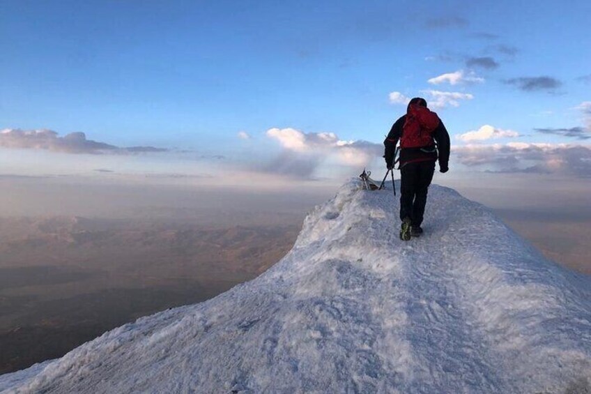 A person hiking on a snow-covered peak with a clear sky and distant landscape. 3