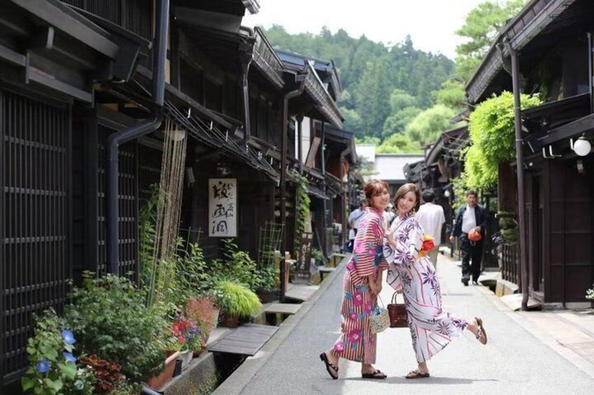 A traditional Japanese street with wooden buildings, a narrow pathway, and greenery. 1