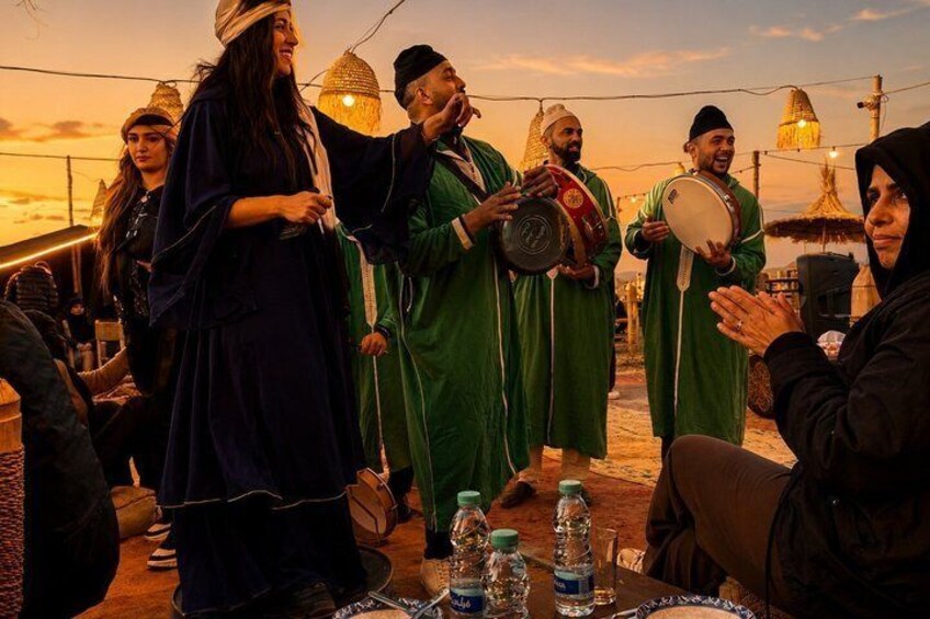 A group of people in traditional attire, some holding musical instruments, gathered around a table with bottles. 5