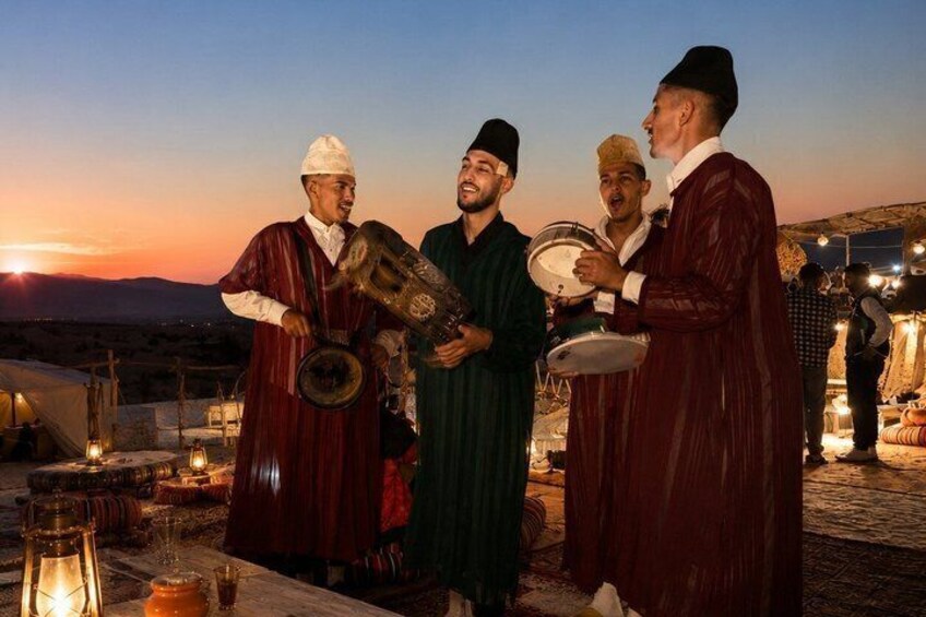 A group of men in traditional attire playing musical instruments, with a sunset in the background. 3