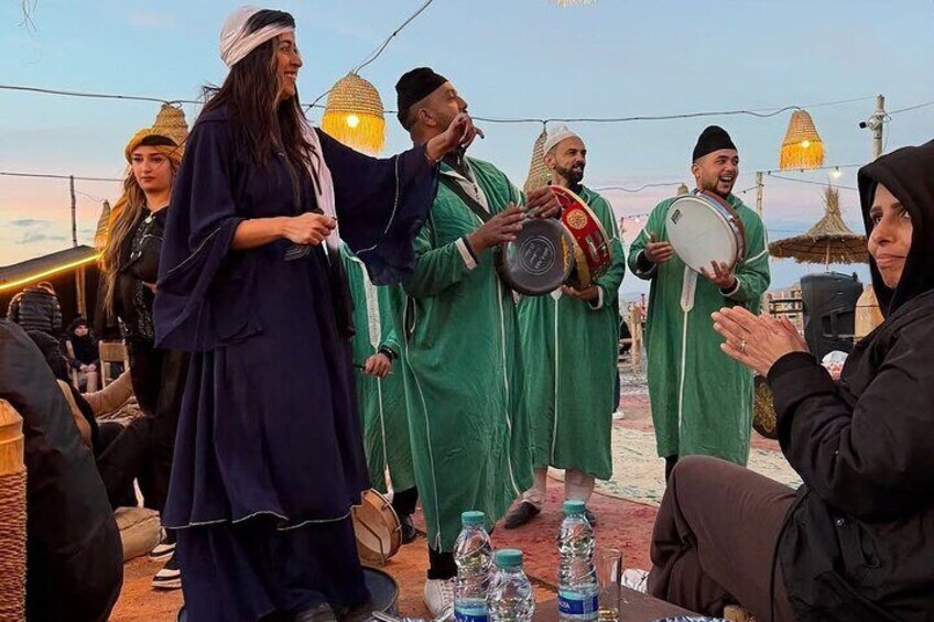 A group of people in traditional attire, some holding musical instruments, gathered in an outdoor setting with string lights. 2