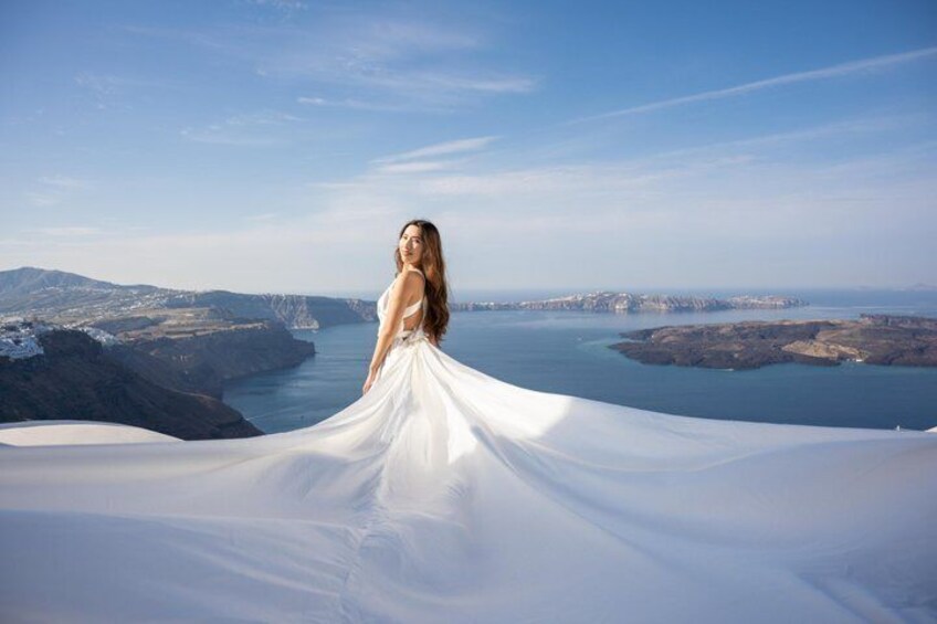 A person in a white dress standing on a cliff overlooking a coastal landscape with mountains and a body of water. 2