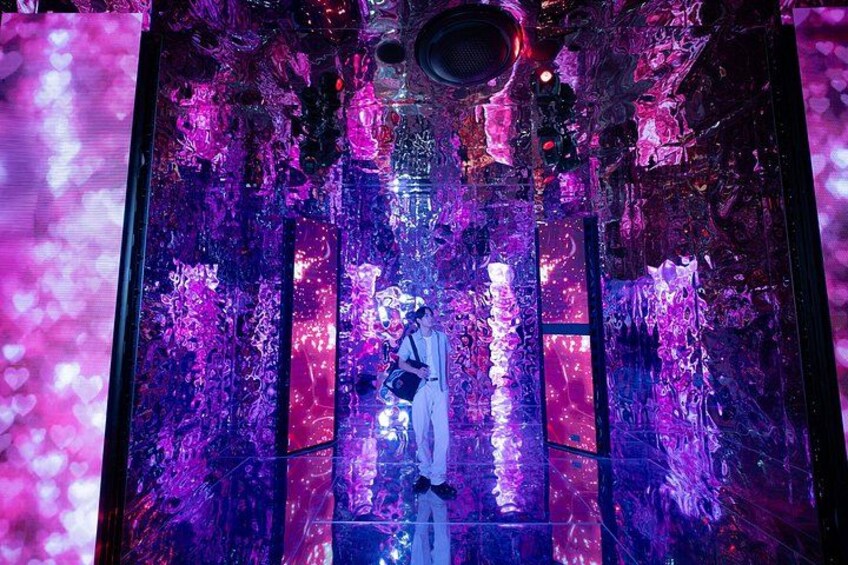 A person in a white outfit standing in a room with a reflective, colorful surface. 2