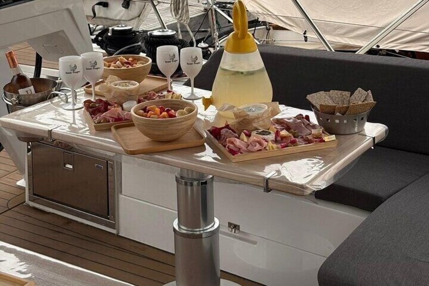 A boat deck with a table set with food, wine glasses, and a baby bottle. 2