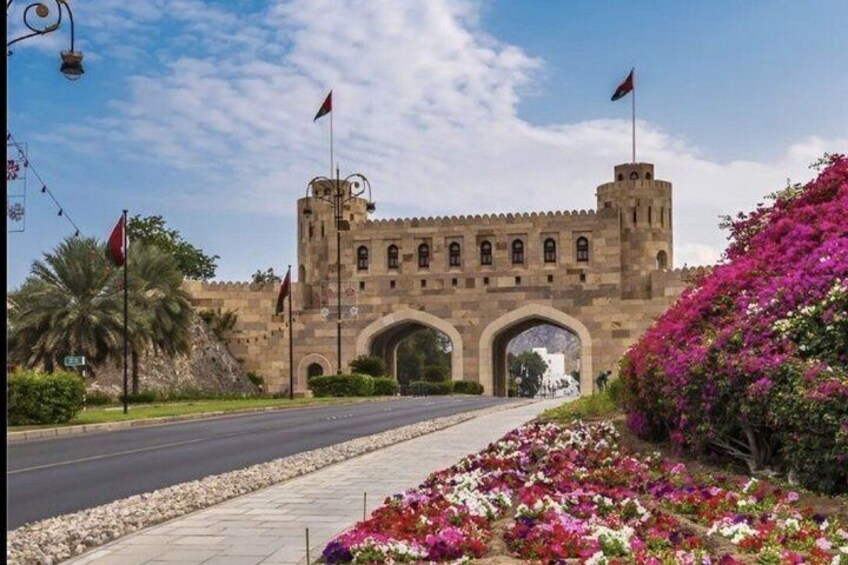 A historic stone building with arches, flags, and vibrant flowers. 1