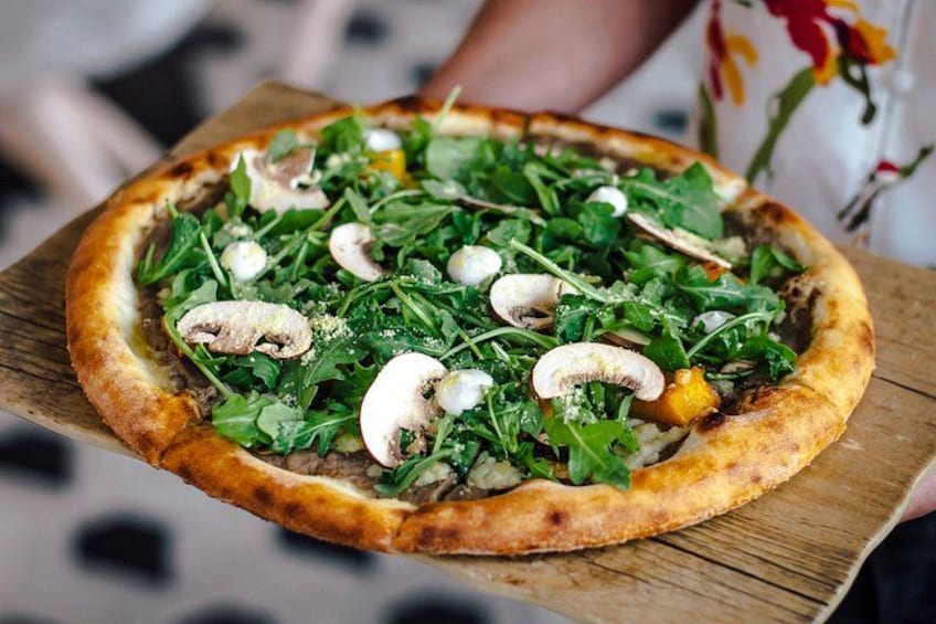 A pizza with greens and mushrooms on a wooden board. 3