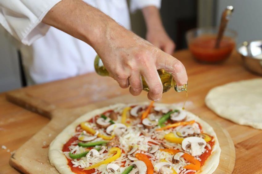 A person preparing a pizza with various toppings on a wooden board. 4
