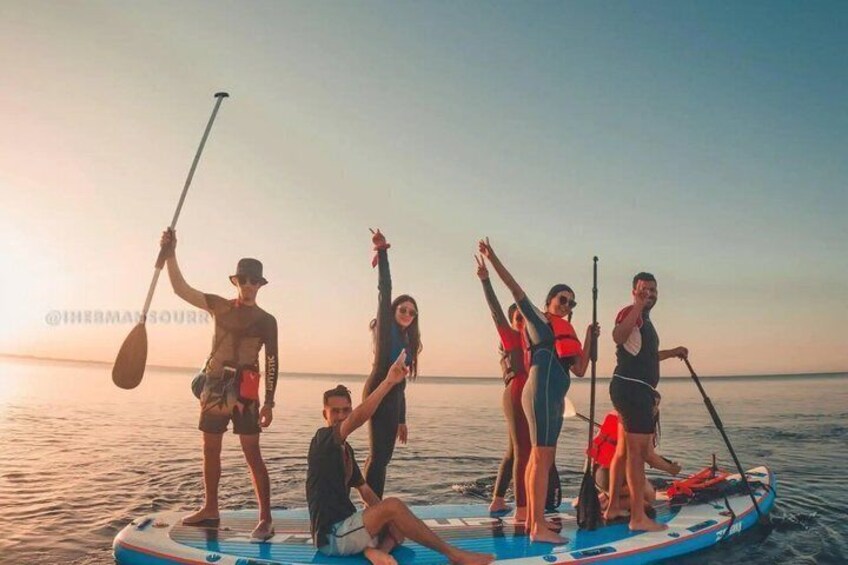 A group of people on a paddleboard in the water during sunset. 1