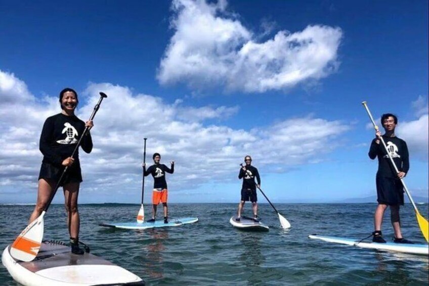 Four people paddleboarding on the water with surfboards and paddles. 2