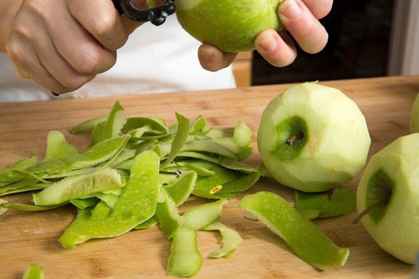 Una persona pelando una manzana sobre una tabla de cortar de madera. 4