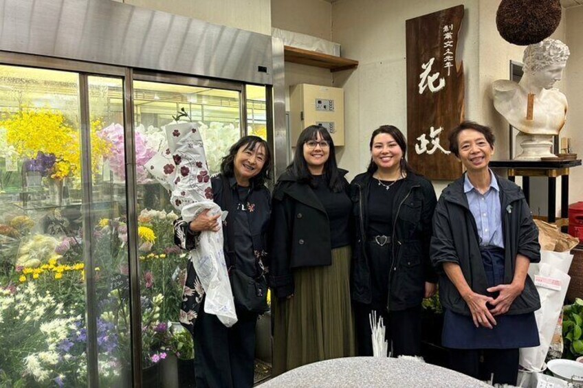A group of people standing indoors with a glass display of flowers and a bust sculpture. 5