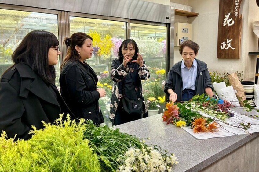 A group of people at a florist counter with various flowers and plants. 1