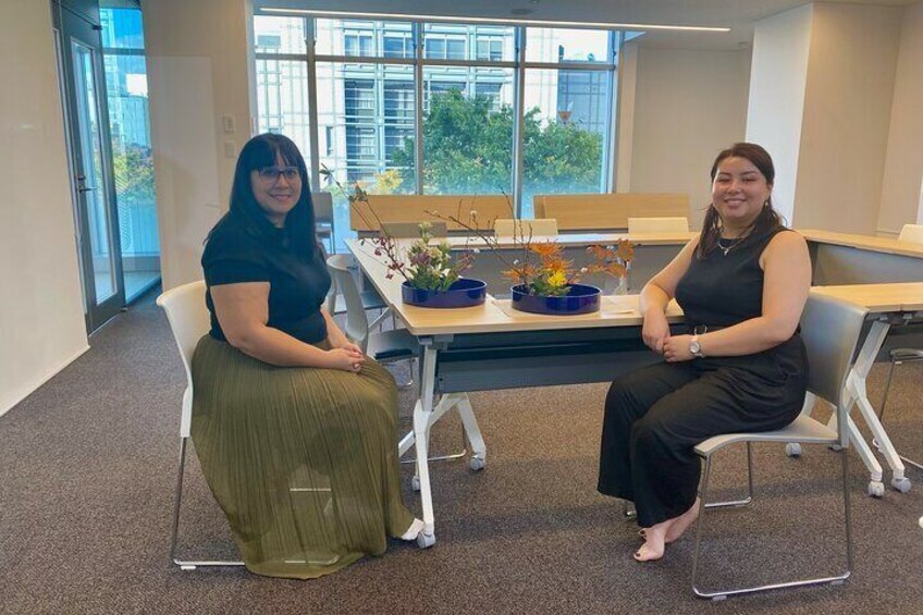Two women seated at a table with a vase of flowers in an office setting. 2