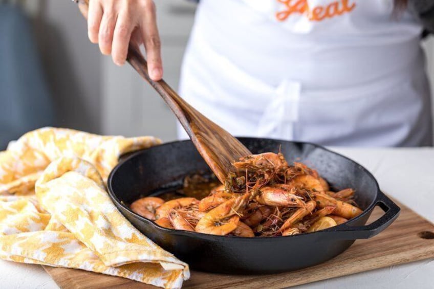 A person cooking shrimp in a skillet on a wooden board. 2