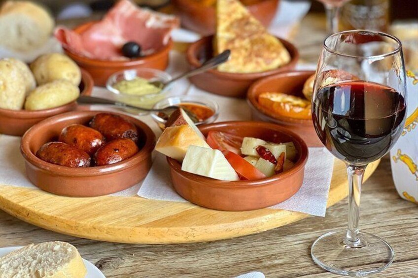 A variety of tapas dishes and a glass of red wine on a wooden table. 5