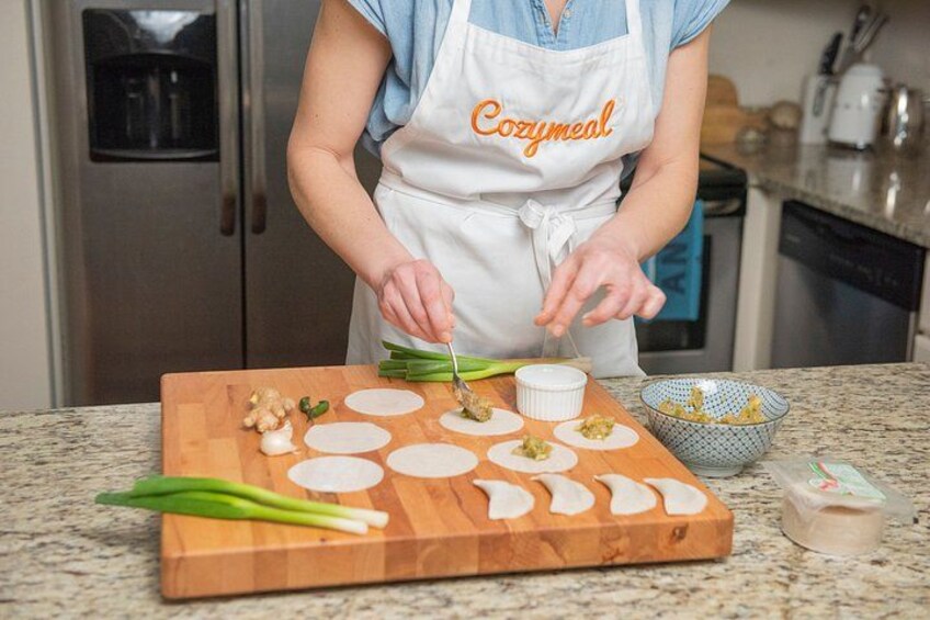 A person preparing food with a cutting board, a bowl, and a container on a kitchen counter. 1