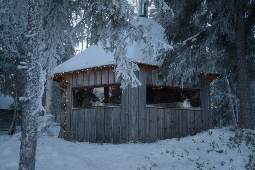 A wooden cabin with snow-covered roof and windows, surrounded by snow-laden trees. 2