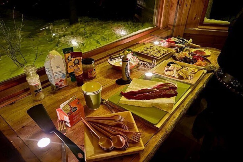 Een houten tafel met verschillende soorten eten en kruiden, verlicht met kaarsen. 4