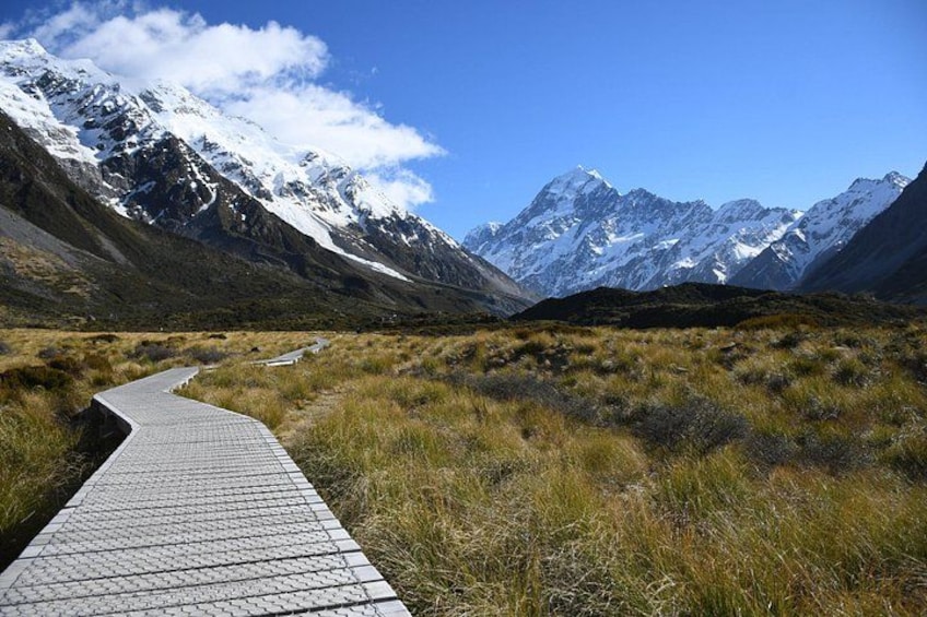 A paved path leading through a mountainous landscape with snow-capped peaks in the background. 2