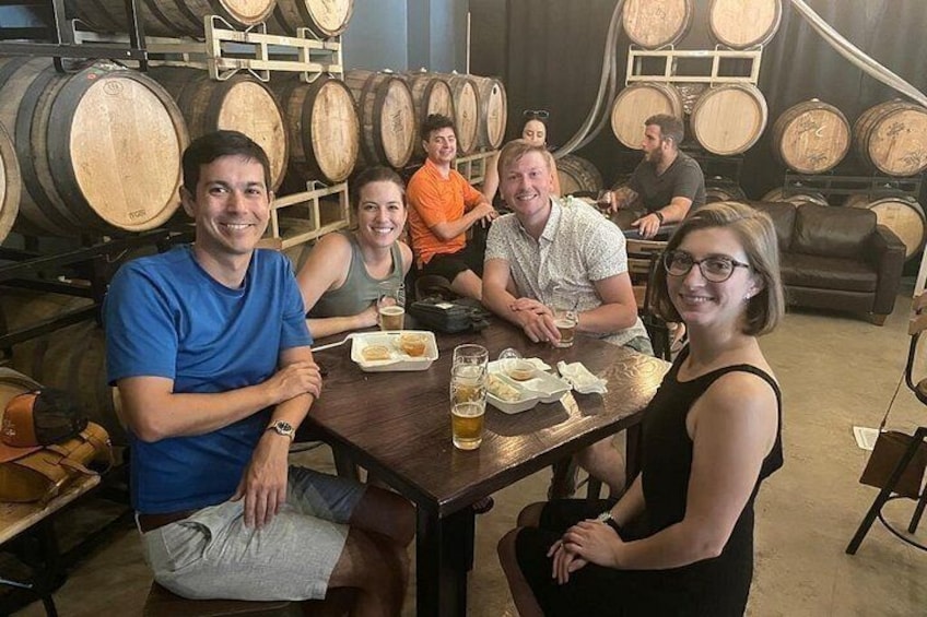 A group of people seated at a table in a cellar with wine barrels in the background. 3