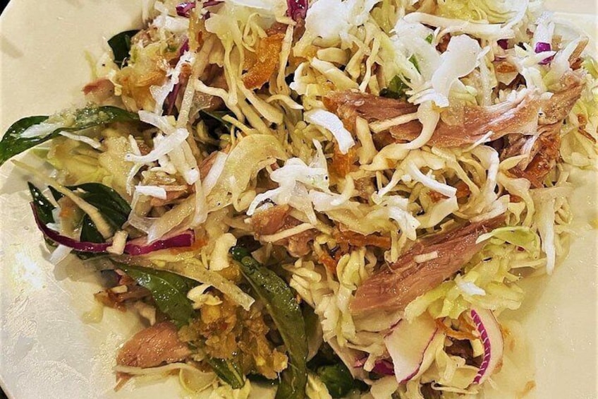A plate of shredded cabbage salad with shredded meat and green leaves. 2