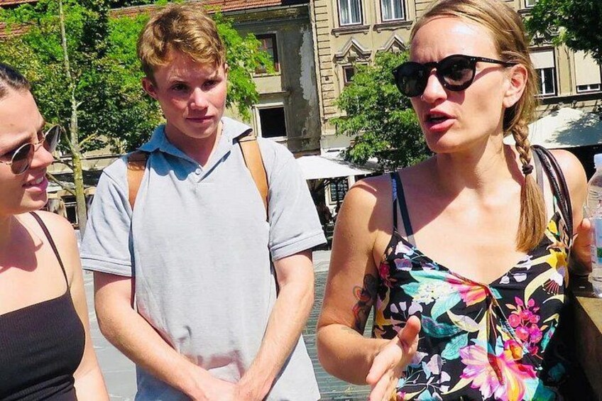 Drei Personen stehen draußen, mit Gebäuden und Bäumen im Hintergrund. 2