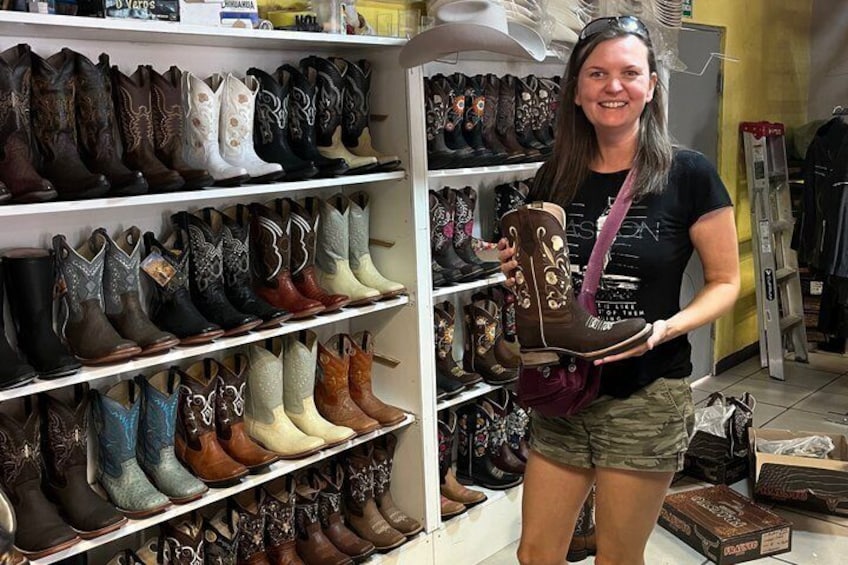 A person holding a cowboy boot in a store with shelves of various boots. 1