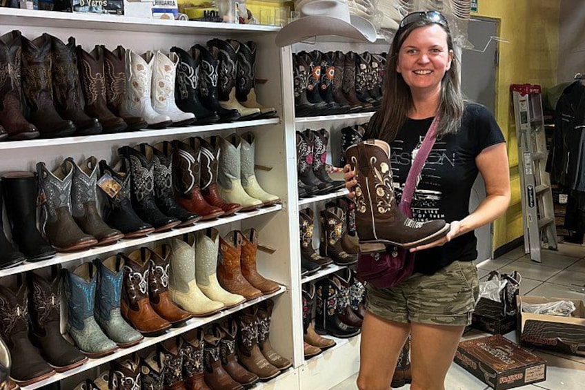 A person holding a cowboy boot in a store with shelves of various boots. 1