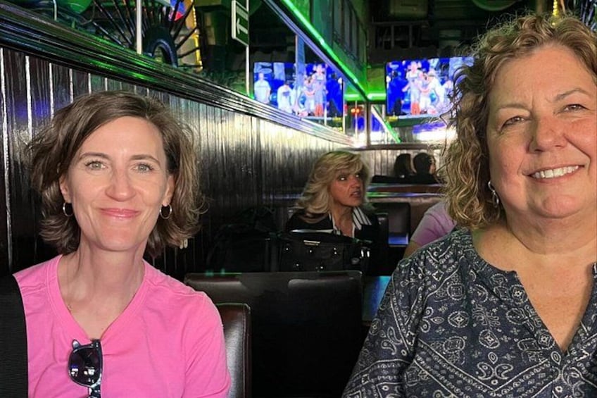 Two people seated in a bar with televisions displaying sports events in the background. 2