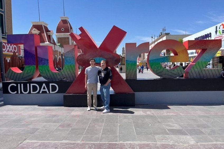 A large colorful sign with the word 'CIUDAD' and two people standing in front of it. 3