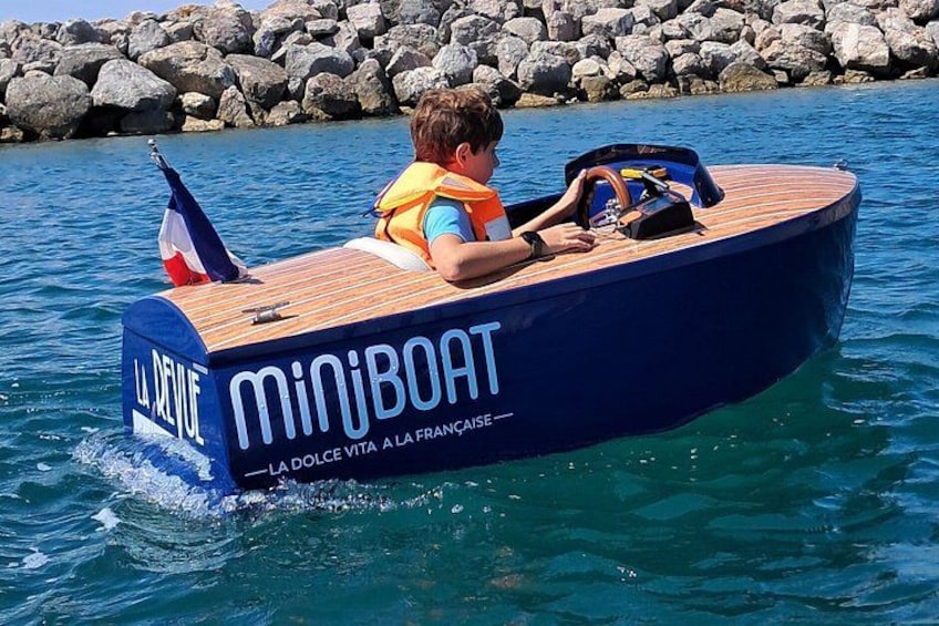 A person in a blue boat with 'miniboot' written on it, floating on water. 1