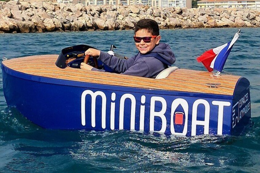 A person in a blue and wooden boat with 'MiniBoat' written on it, floating on water. 2
