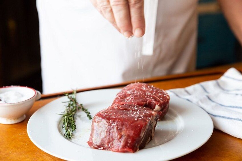 Une personne assaisonne un steak cru avec du sel sur une assiette blanche. 5