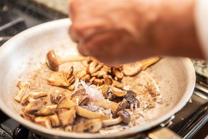 A hand seasoning mushrooms in a pan. 2