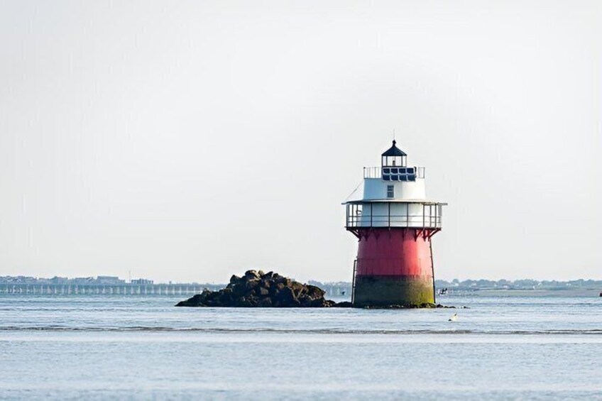 A lighthouse on a small island with calm water and a pier in the background. 3