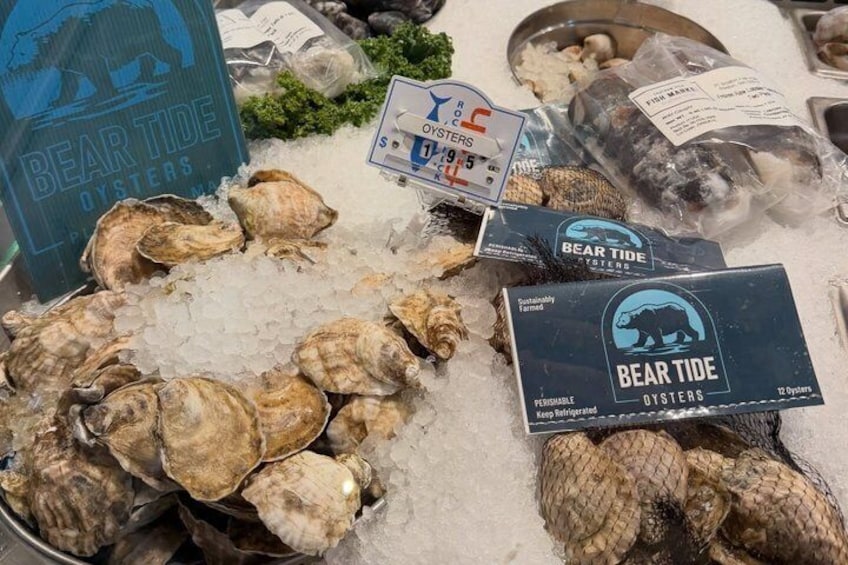 A display of oysters on ice with labels indicating 'Bear Tide Oysters' and a 'Keep Refrigerated' sign. 1