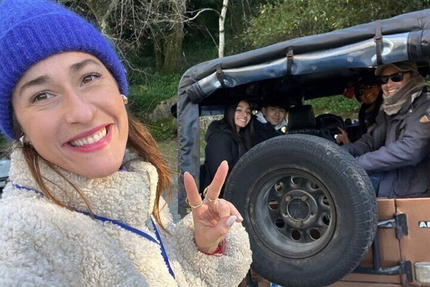 A person in a blue beanie and white fleece jacket posing with a peace sign in front of a vehicle. 1