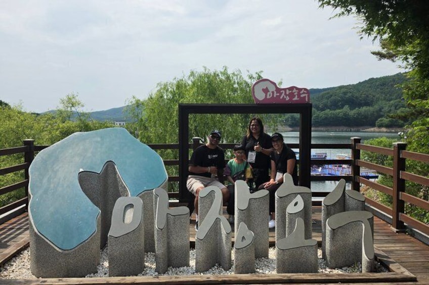 Un groupe de personnes se trouve sur un pont en bois, à proximité d’un panneau indicateur et d’une grande sculpture en pierre. 2